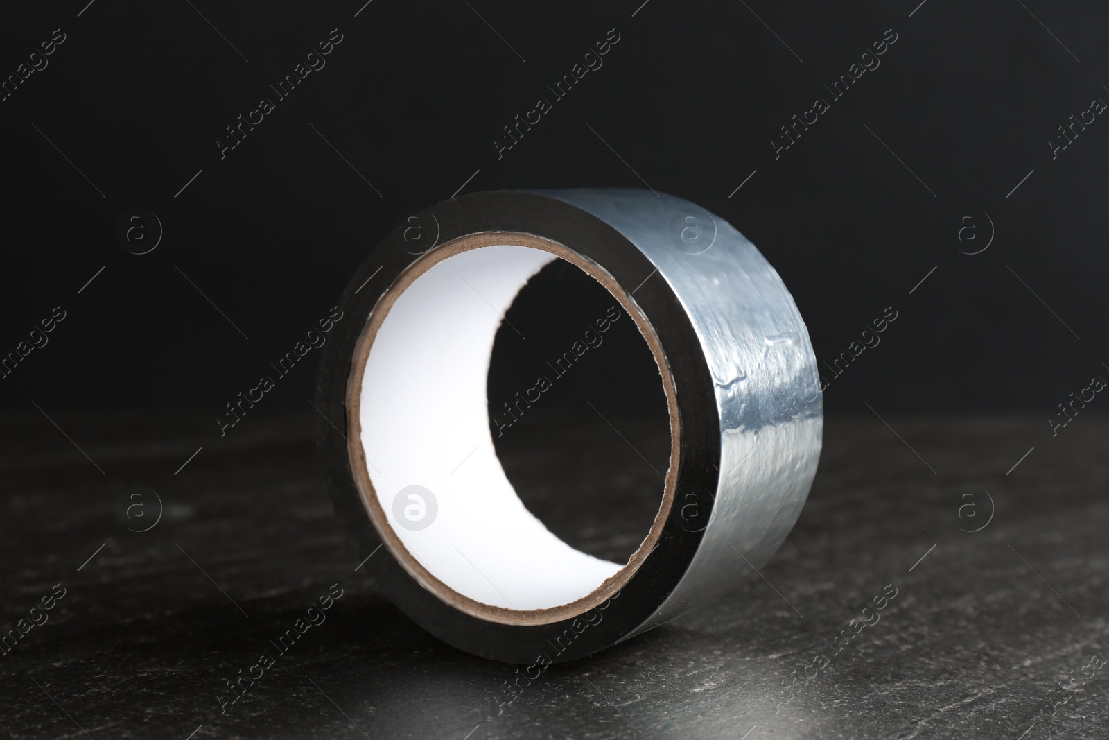 Photo of Roll of silver adhesive tape on black table, closeup