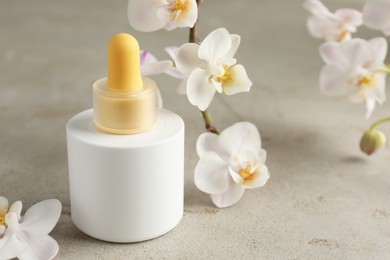 Photo of Bottle of skin care product and orchid flowers on gray textured surface