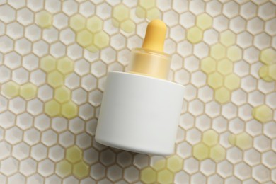 Photo of Bottle of skin care product on beige honeycomb surface, top view