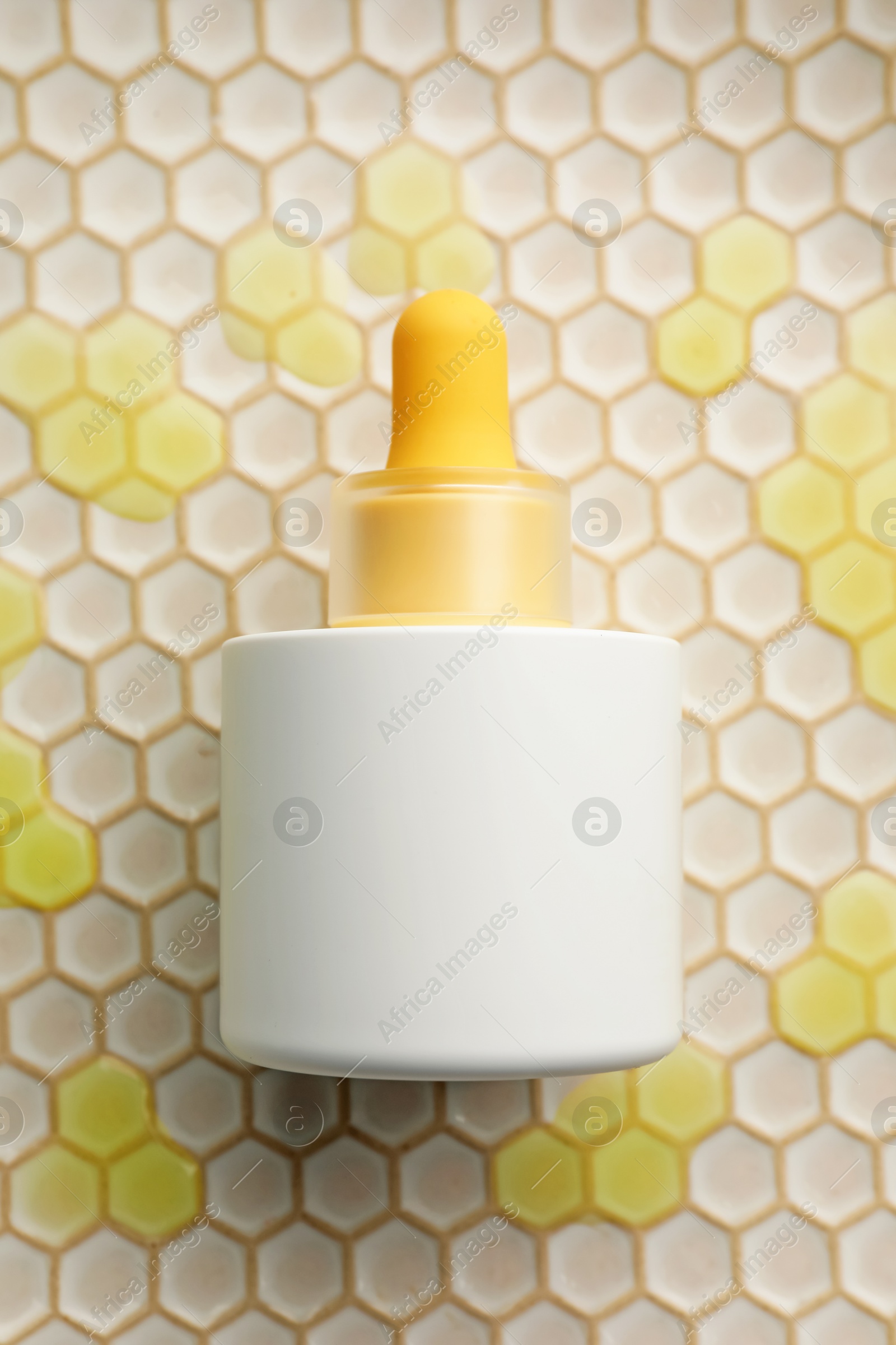 Photo of Bottle of skin care product on beige honeycomb surface, top view