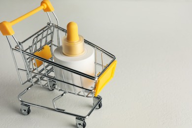 Photo of Bottle of skin care product in small shopping cart on light background, space for text