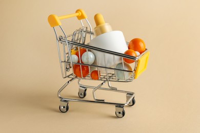 Photo of Bottle of skin care product and colorful balls in small shopping cart on beige background