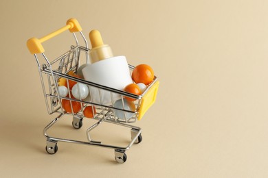 Photo of Bottle of skin care product and colorful balls in small shopping cart on beige background, space for text