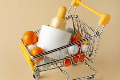 Photo of Bottle of skin care product and colorful balls in small shopping cart on beige background, closeup