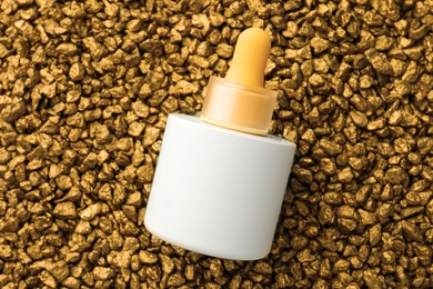 Photo of Bottle of skin care product on gold nuggets, top view