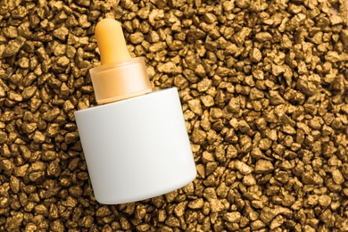 Photo of Bottle of skin care product on gold nuggets, top view. Space for text