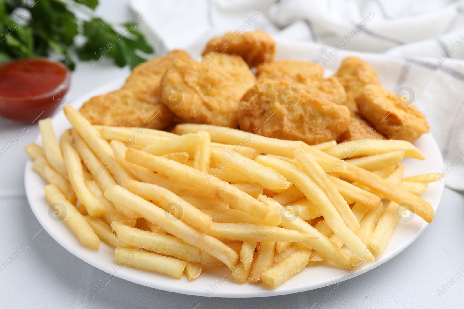 Tasty chicken nuggets and french fries with sauce on white tiled table, closeup Photo of Tasty chicken nuggets and french fries with sauce on white tiled table, closeup