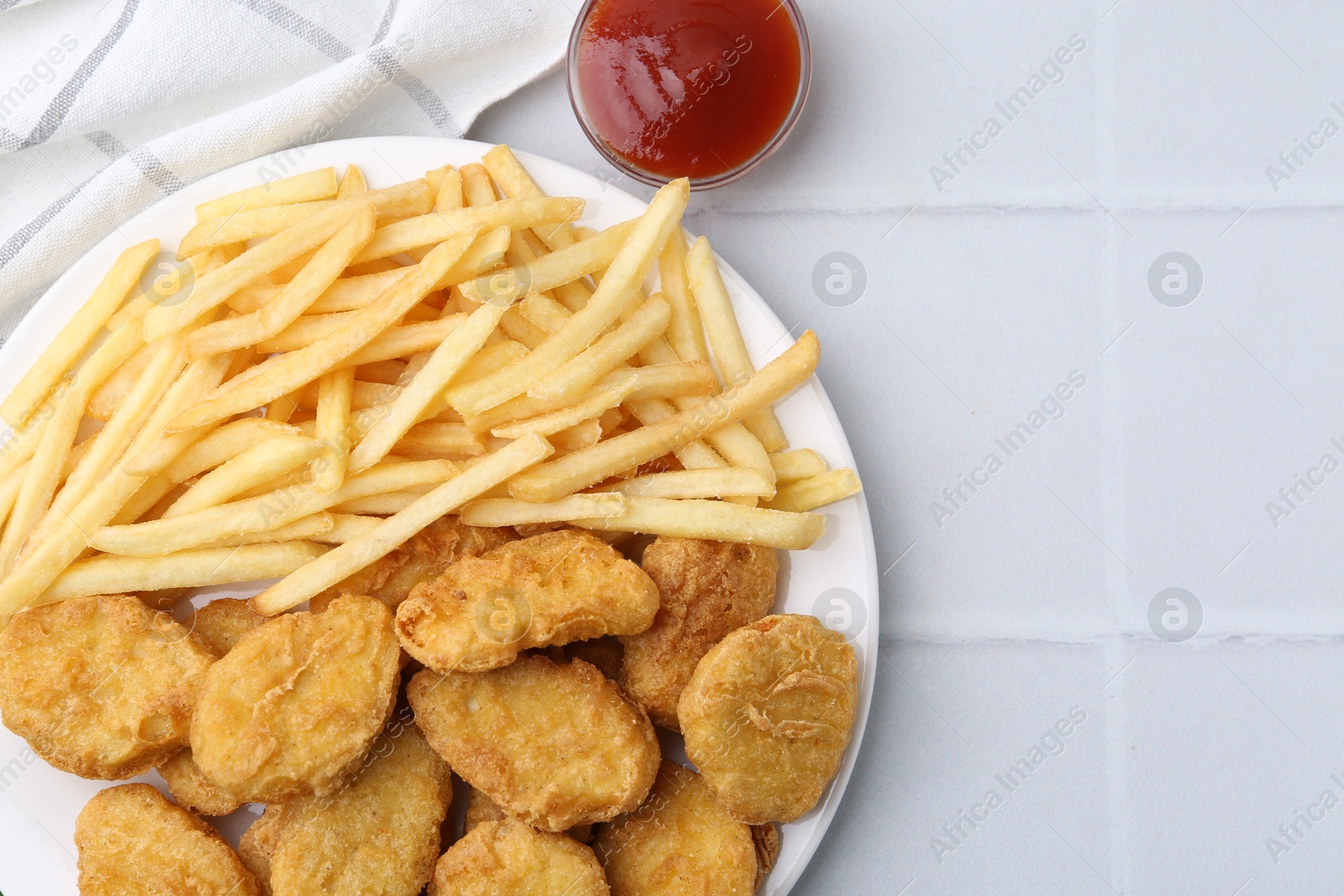 Tasty chicken nuggets and french fries with sauce on white tiled table, flat lay. Space for text Photo of Tasty chicken nuggets and french fries with sauce on white tiled table, flat lay. Space for text