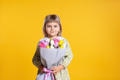 Photo of Cute little girl with bouquet of tulips on orange background