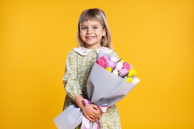 Photo of Smiling little girl with bouquet of tulips on orange background