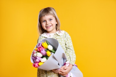 Photo of Smiling little girl with bouquet of tulips on orange background