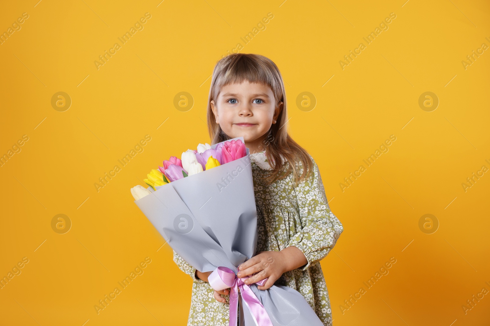 Photo of Cute little girl with bouquet of tulips on orange background