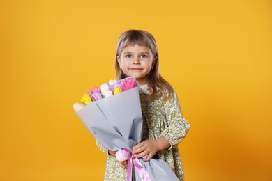 Photo of Cute little girl with bouquet of tulips on orange background