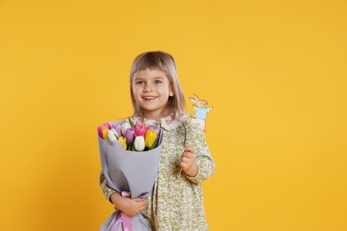 Photo of Smiling little girl with bouquet of tulips and decorative Easter bunny on orange background