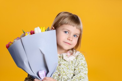 Photo of Cute little girl with bouquet of tulips on orange background