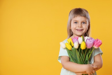 Photo of Smiling little girl with bouquet of tulips on yellow background. Space for text