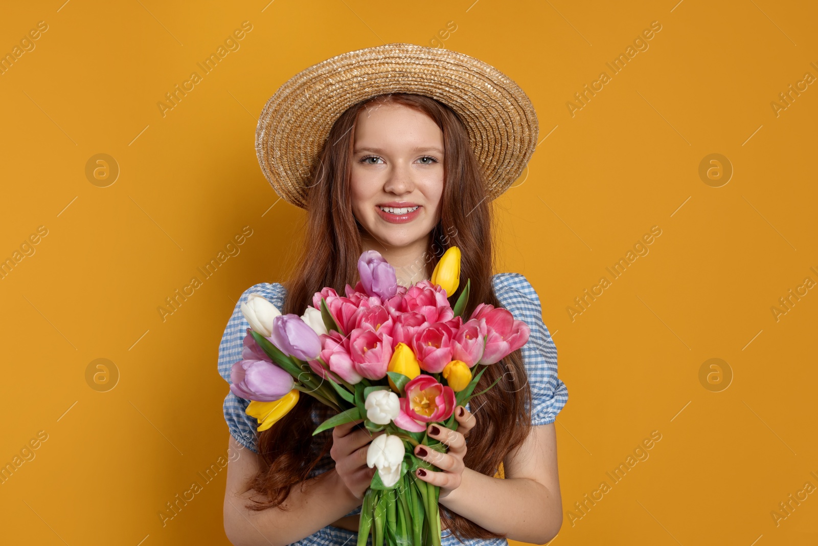 Photo of Beautiful teenage girl with bouquet of tulips on orange background