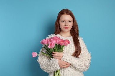 Photo of Beautiful teenage girl with bouquet of tulips on light blue background