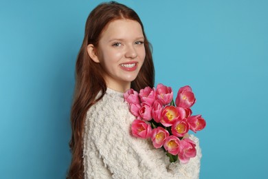 Photo of Beautiful teenage girl with bouquet of tulips on light blue background