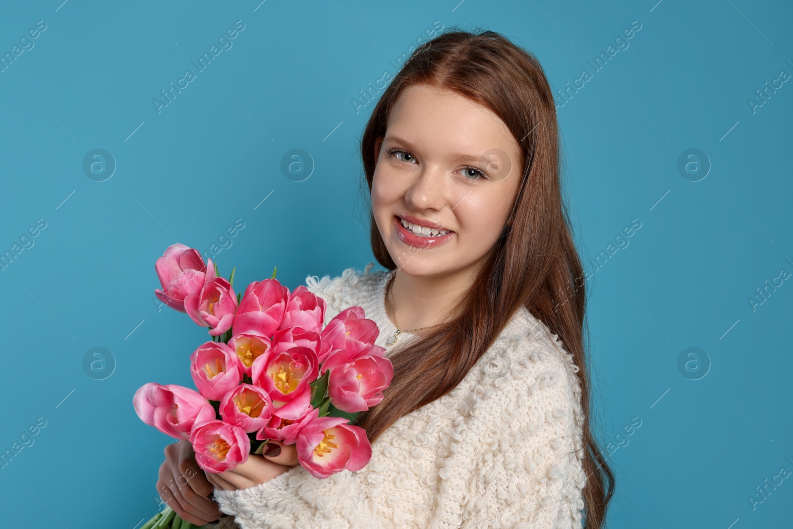 Photo of Beautiful teenage girl with bouquet of tulips on light blue background