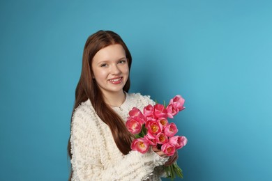 Photo of Beautiful teenage girl with bouquet of tulips on light blue background