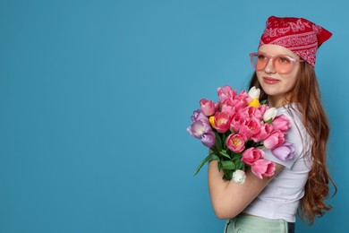 Photo of Beautiful teenage girl with bouquet of tulips on light blue background, space for text