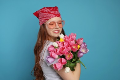 Photo of Beautiful teenage girl with bouquet of tulips on light blue background