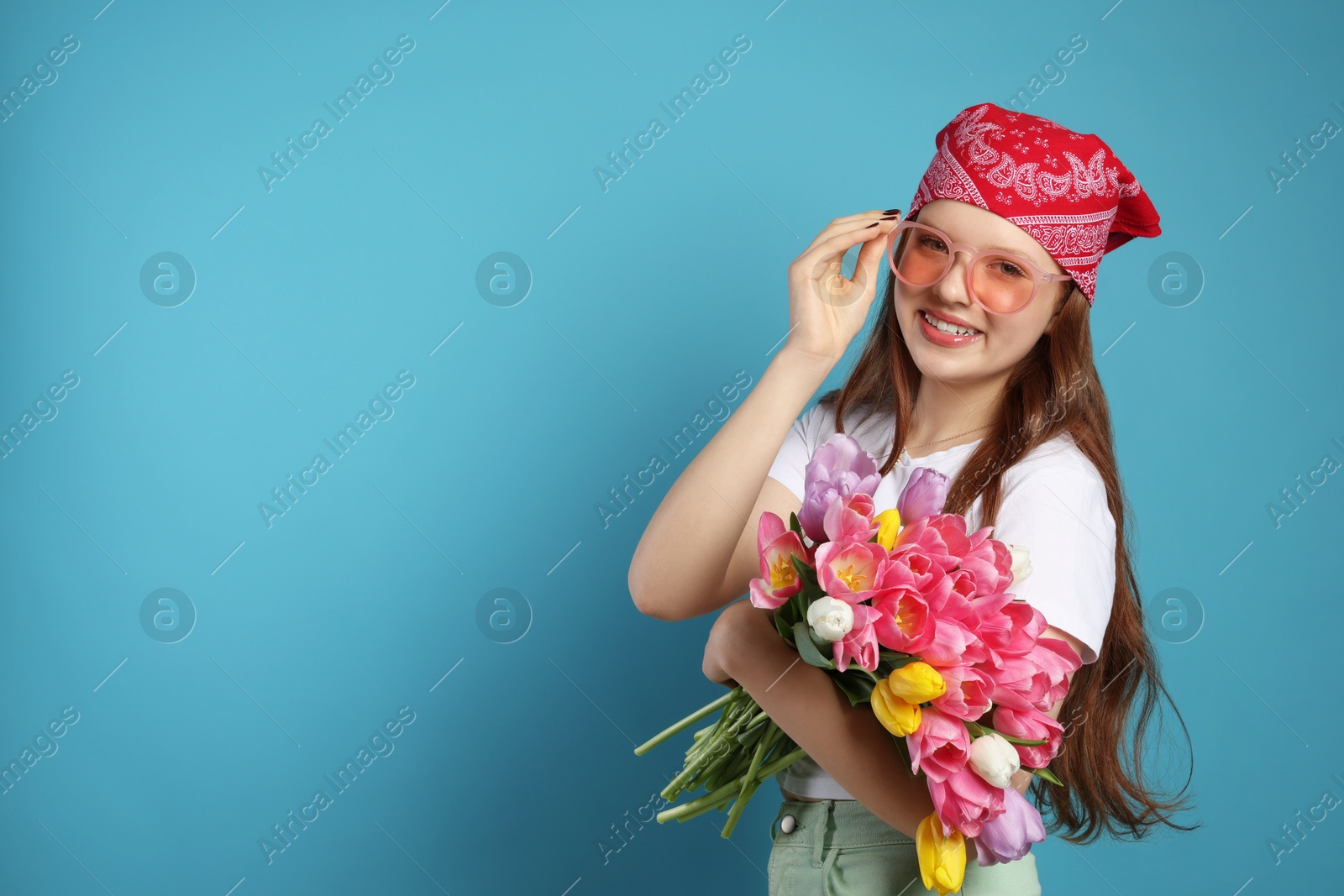 Photo of Beautiful teenage girl with bouquet of tulips on light blue background, space for text