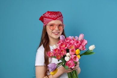 Photo of Beautiful teenage girl with bouquet of tulips on light blue background