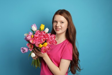 Photo of Beautiful teenage girl with bouquet of tulips on light blue background