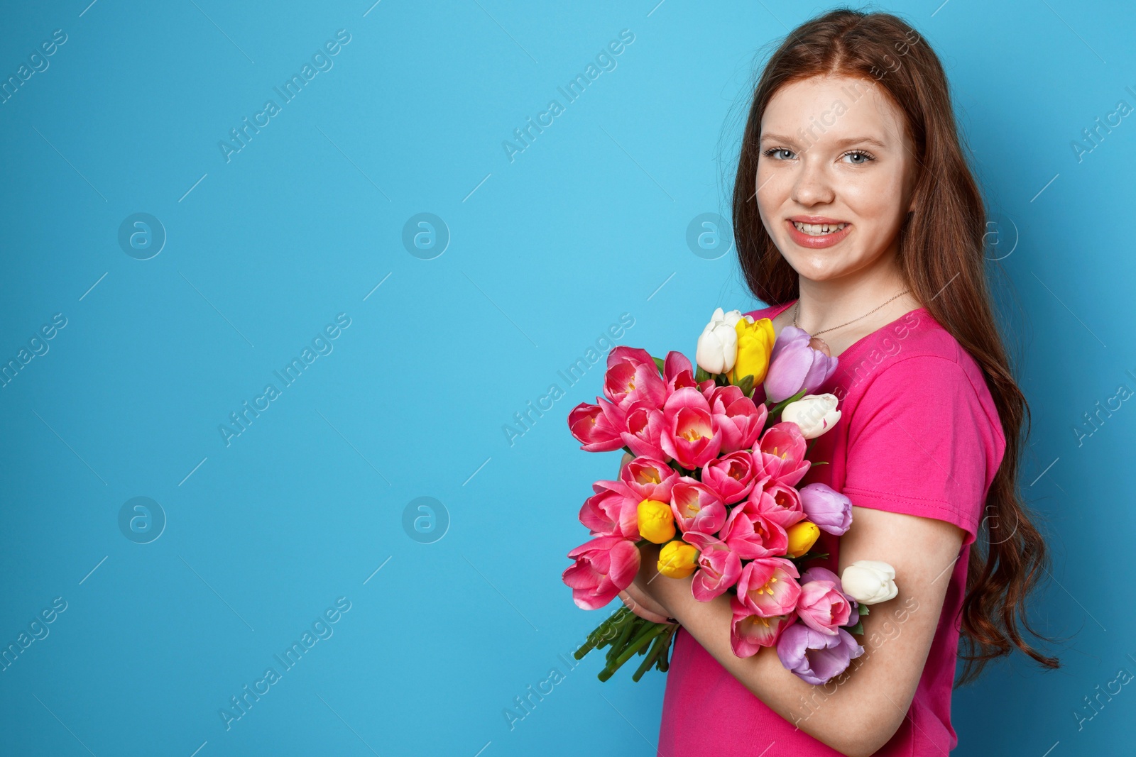 Photo of Beautiful teenage girl with bouquet of tulips on light blue background, space for text