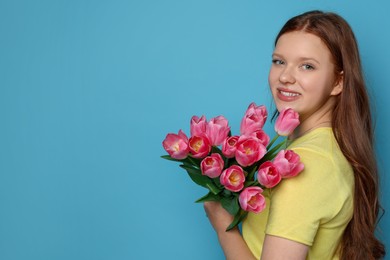 Photo of Beautiful teenage girl with bouquet of tulips on light blue background, space for text