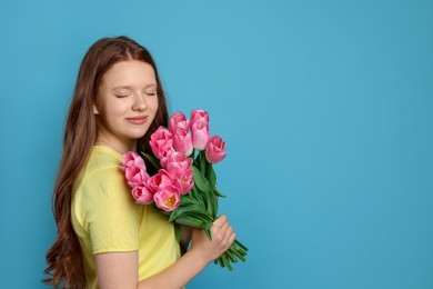 Photo of Beautiful teenage girl with bouquet of tulips on light blue background, space for text