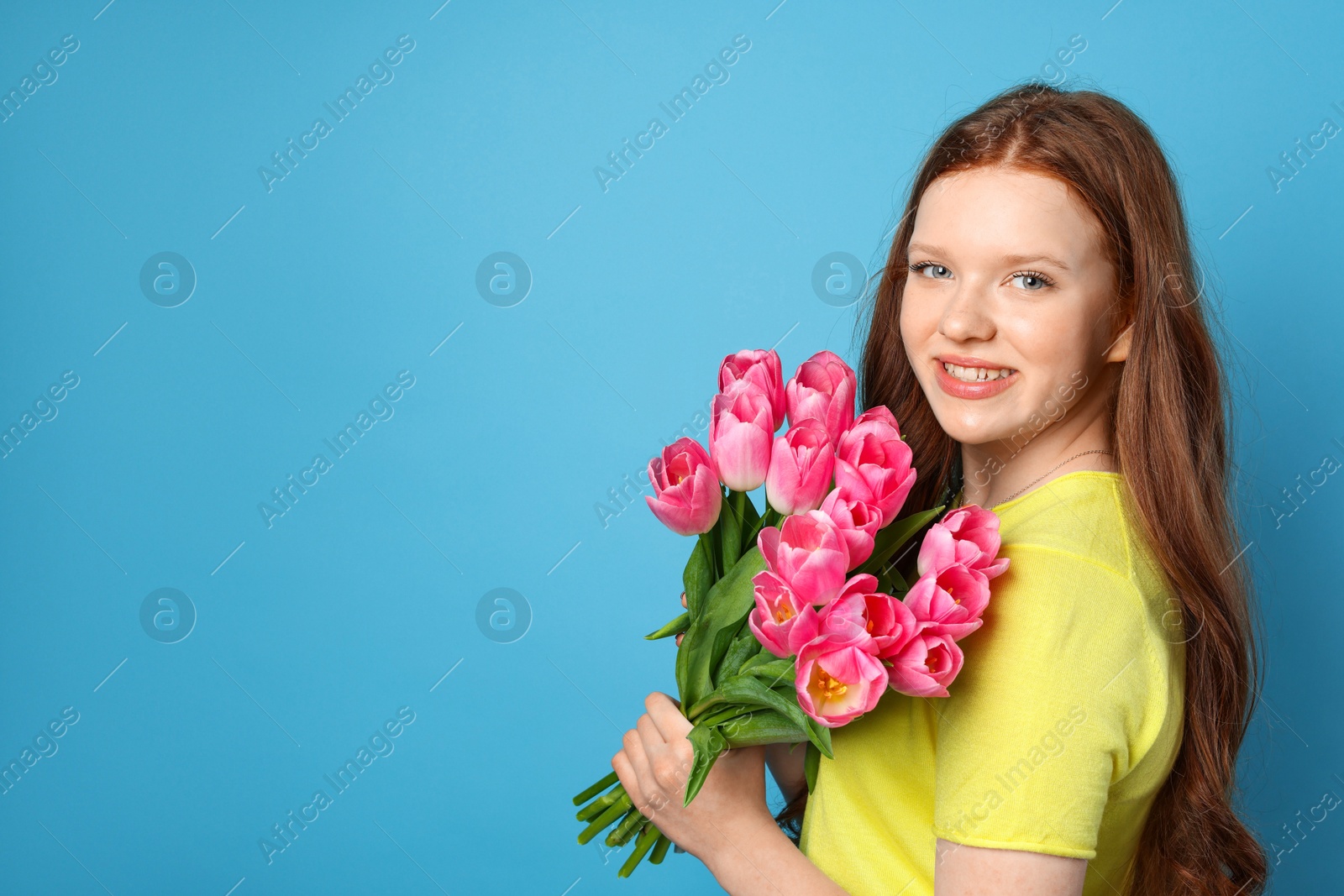 Photo of Beautiful teenage girl with bouquet of tulips on light blue background, space for text