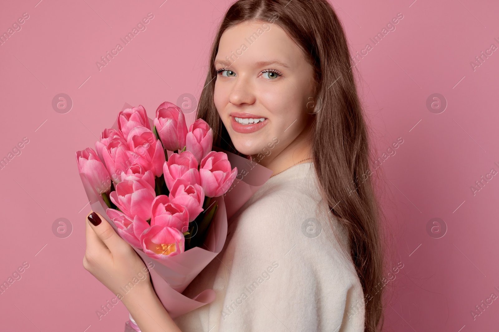 Photo of Beautiful teenage girl with bouquet of tulips on pink background