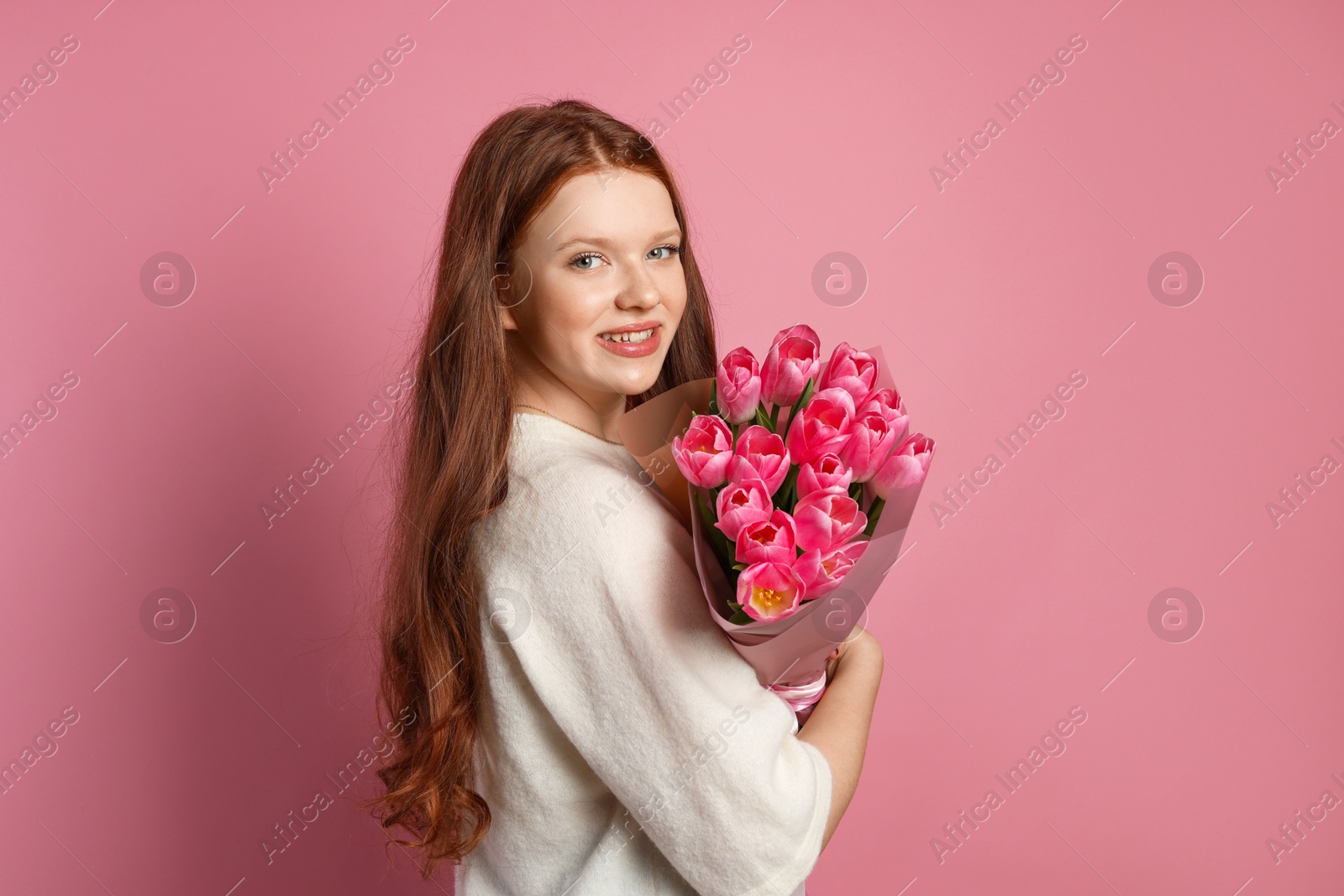 Photo of Beautiful teenage girl with bouquet of tulips on pink background