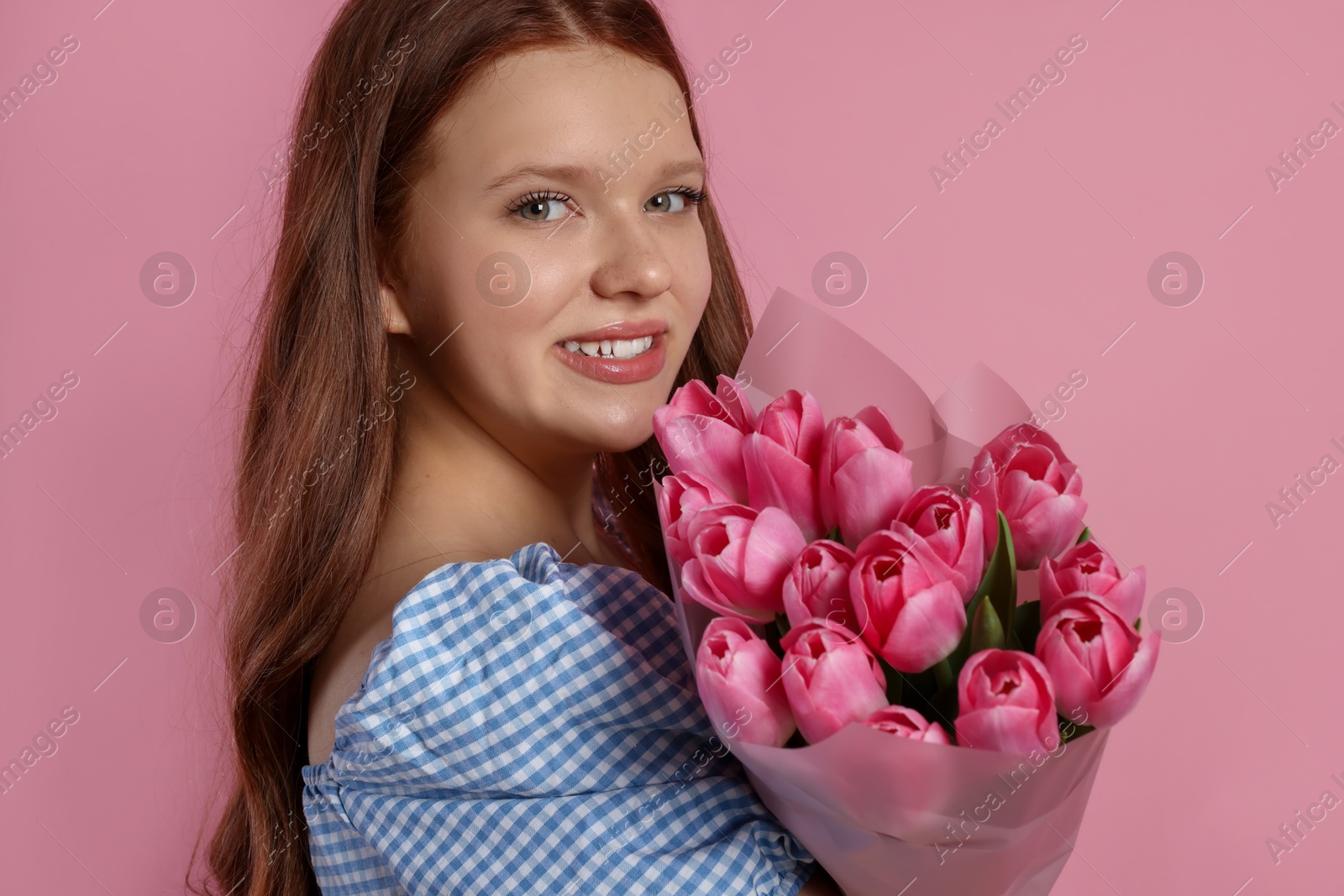 Photo of Beautiful teenage girl with bouquet of tulips on pink background