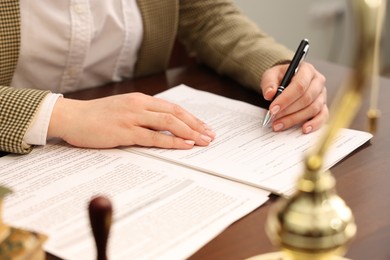 Photo of Notary signing document at table in office, closeup