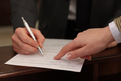 Photo of Notary showing client where to sign document in office, closeup