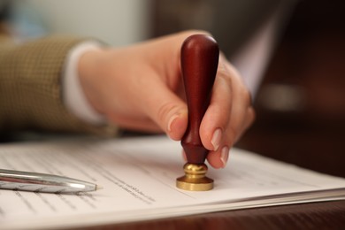 Photo of Notary stamping document at table in office, closeup