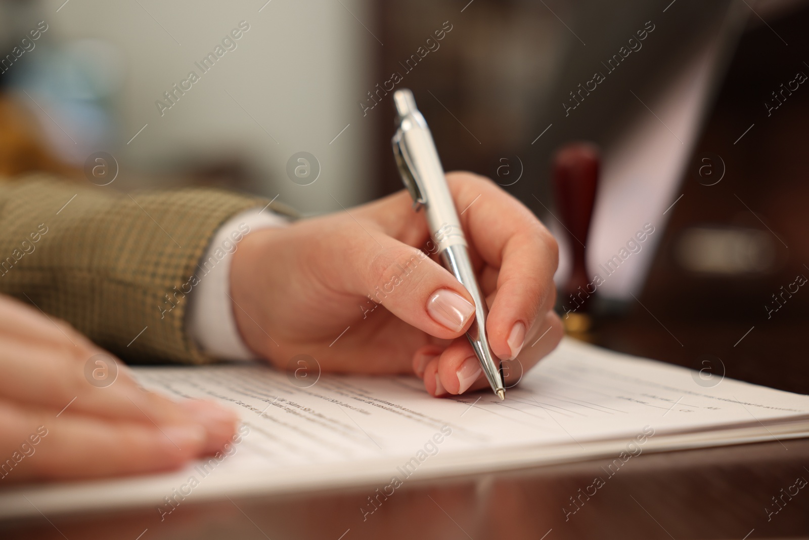 Photo of Notary signing document at table in office, closeup