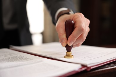 Photo of Notary stamping document at table in office, closeup