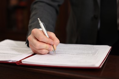 Photo of Notary signing document at table in office, closeup