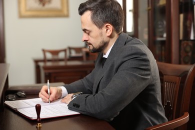 Photo of Notary signing document at table in office