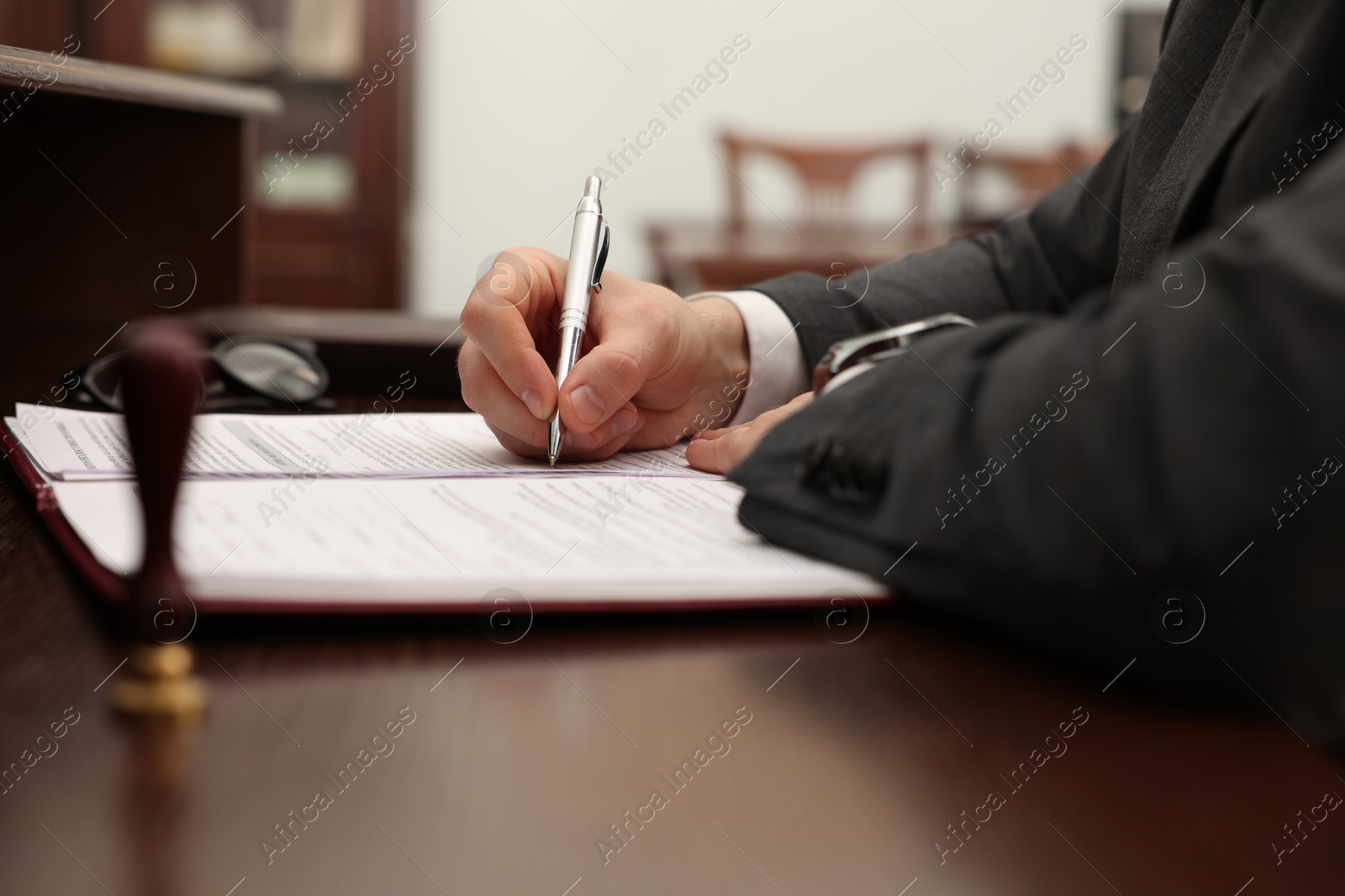 Photo of Notary signing document at table in office, closeup