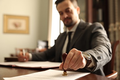 Photo of Notary stamping document at table in office, selective focus