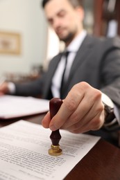 Photo of Notary stamping document at table in office, selective focus