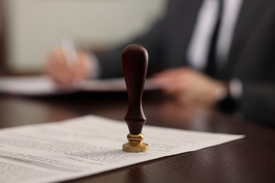 Photo of Notary working at wooden table in office, focus on stamp