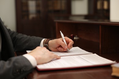 Photo of Notary signing document at table in office, closeup