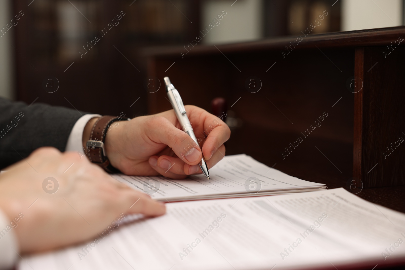 Photo of Notary signing document at table in office, closeup